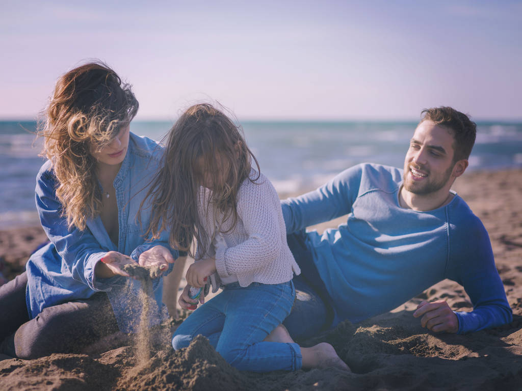 Küçük kızı dinlenen ve sonbahar günü kumsalda eğlenen bir aile. Renkli bir filtre. - Fotoğraf, Görsel