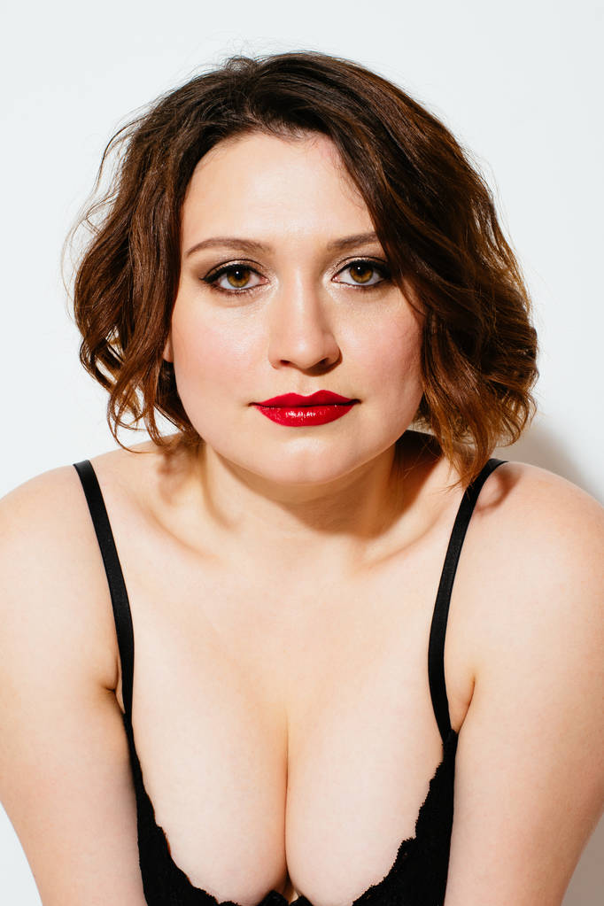 Attractive plus size model with bright makeup wearing black bra and looking at camera on white background - Photo, Image