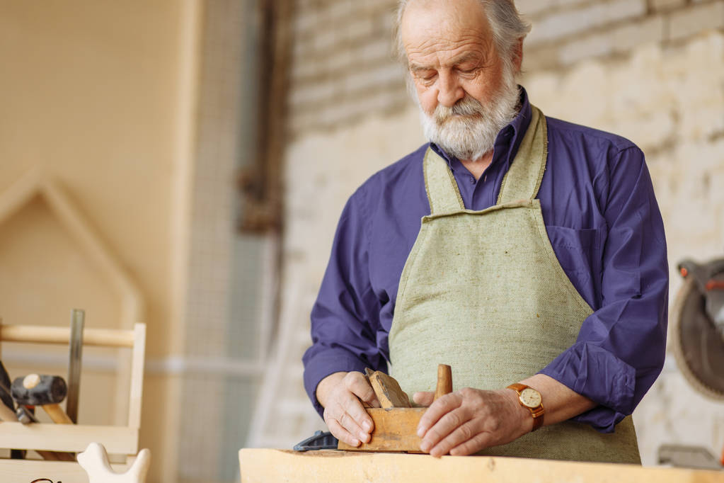 alter erfahrener Tischler arbeitet mit Holzhobel an Dielenwerkstätte. - Foto, Bild