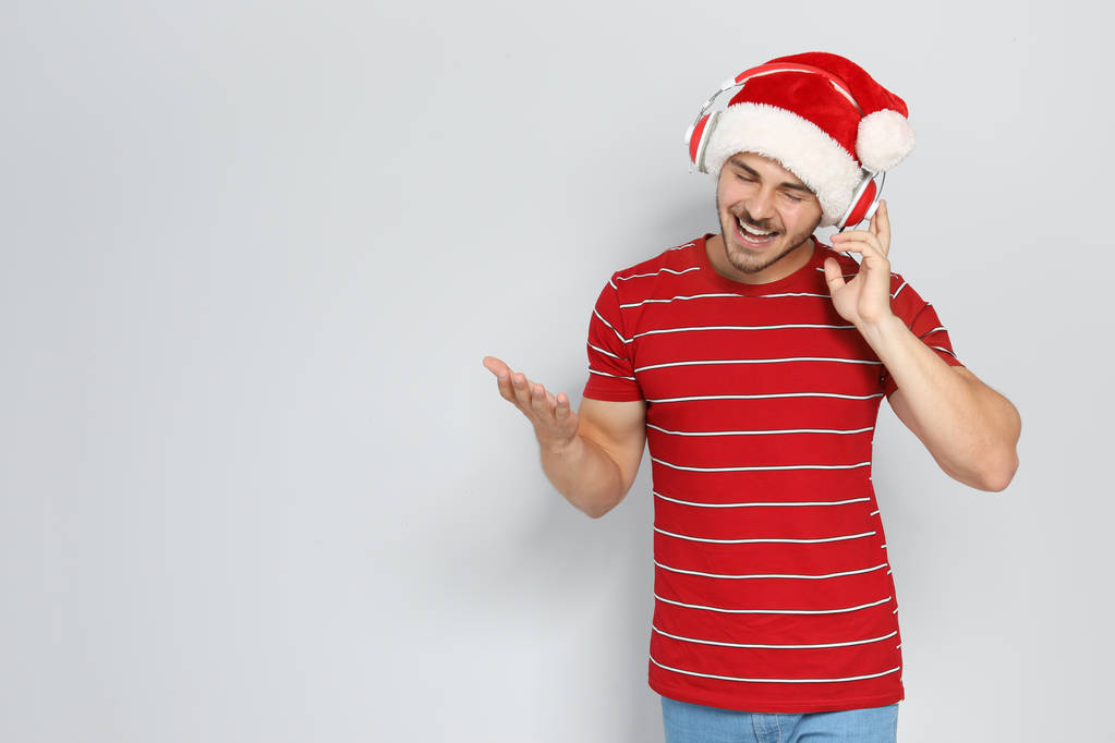junger Mann mit Weihnachtsmütze hört Weihnachtsmusik auf farbigem Hintergrund - Foto, Bild