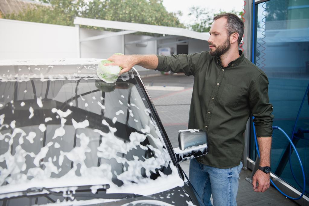 Zijaanzicht van de knappe man auto bij Autowassen met doek en schuim reiniging - Foto, afbeelding