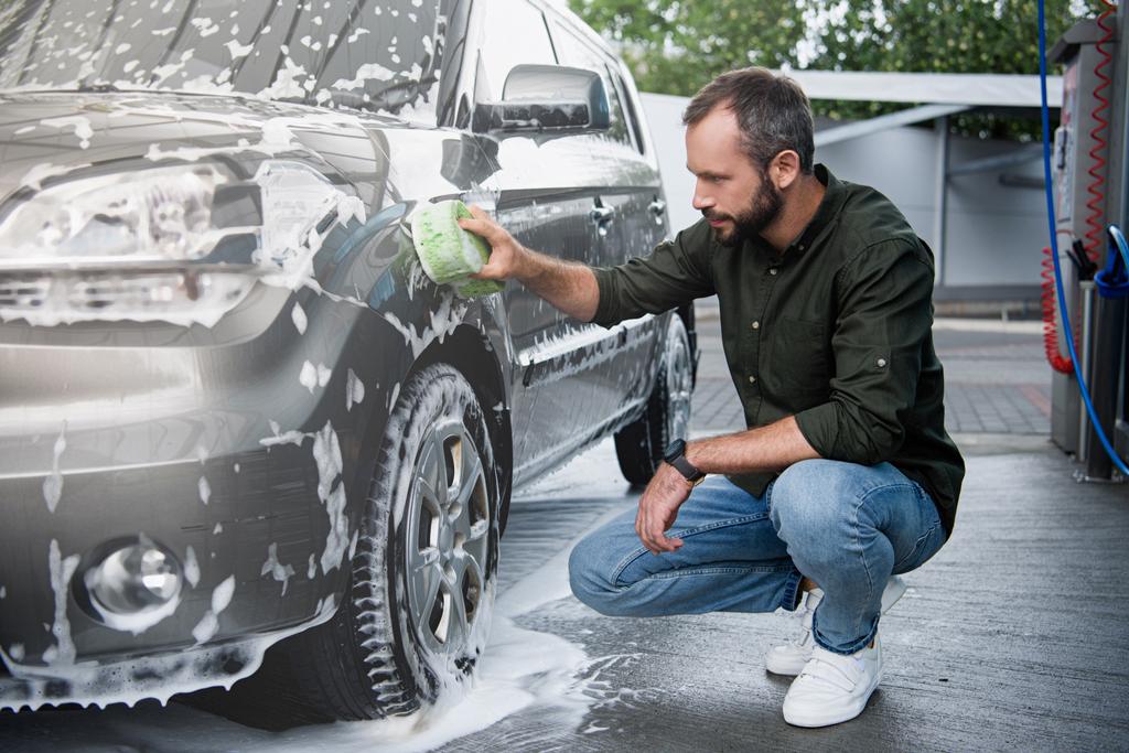 bell'uomo accovacciato e pulizia auto a lavaggio auto con straccio e schiuma
 - Foto, immagini
