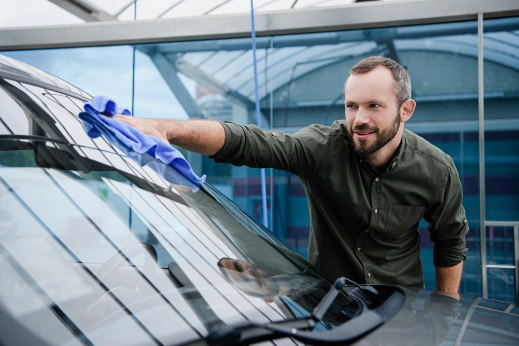 schöner Mann putzt Autoscheibe an Waschanlage mit Lappen  - Foto, Bild