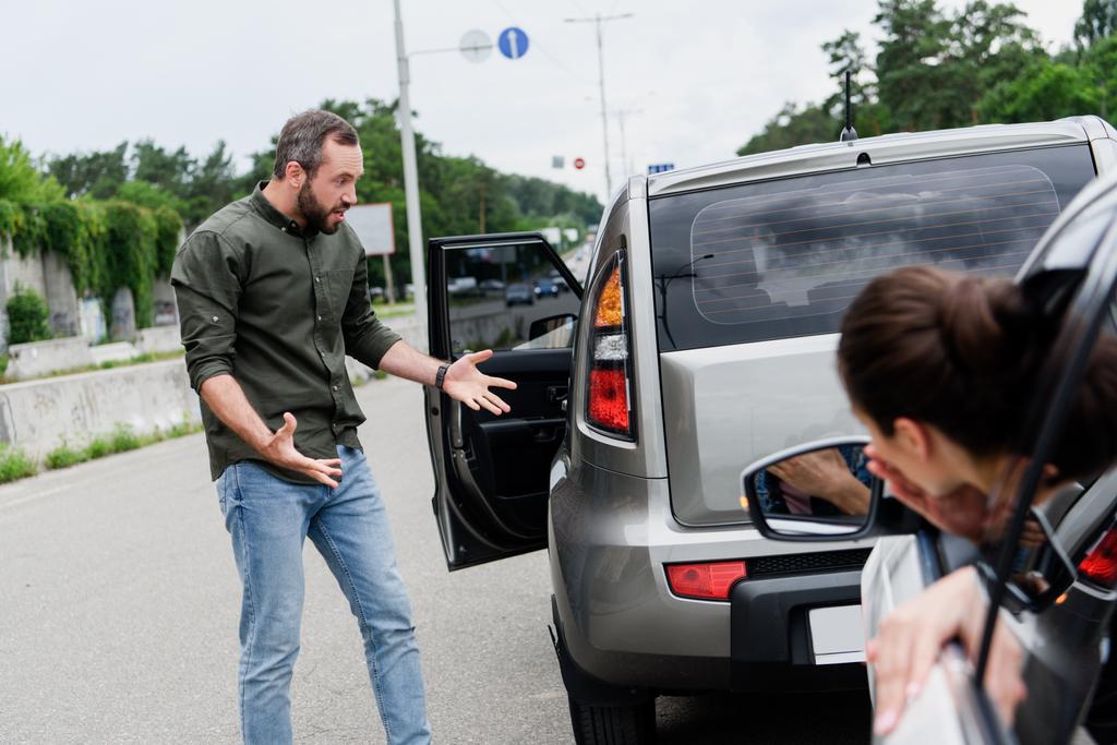 道路上の車の事故後に身振りで示す男性と女性ドライバー - 写真・画像