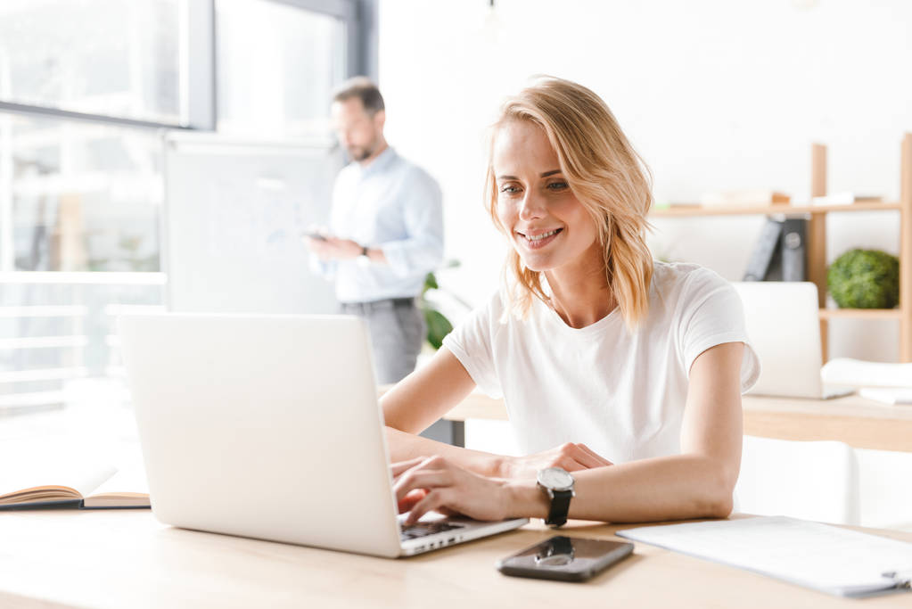 Διαχείριση ελκυστική γυναίκα εργάζεται στον φορητό υπολογιστή ενώ κάθεστε στο γραφείο με co εργαζόμενος άνθρωπος σε φόντο - Φωτογραφία, εικόνα