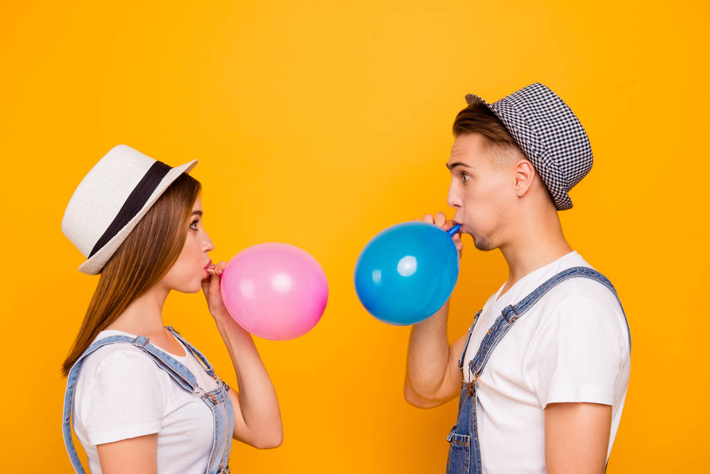 Giovane coppia felice innamorata indossa cappelli che soffiano palloncini d'aria cercando confuso di sfondo giallo, isolato
 - Foto, immagini