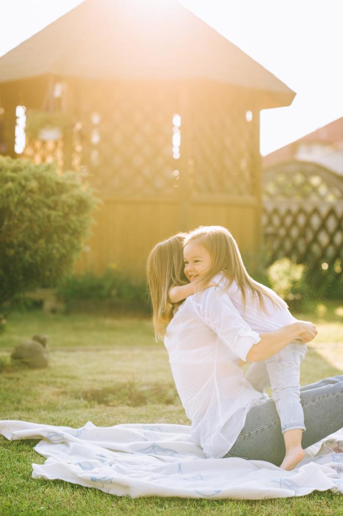 Mutter und glückliche Tochter umarmen sich, während sie gemeinsam auf einem Tuch im Hinterhof ruhen - Foto, Bild