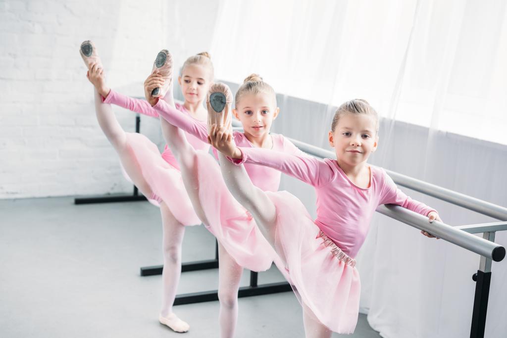 rozkošné děti v růžové tutu sukně cvičí balet a při pohledu na fotoaparát v baletní škole - Fotografie, Obrázek