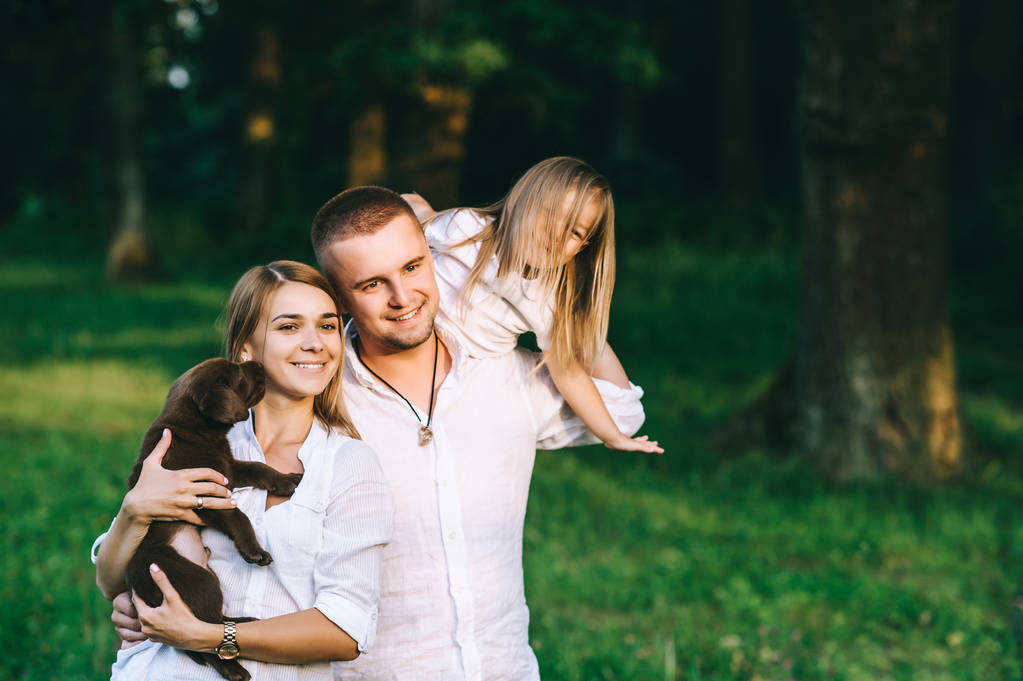 портрет щасливої сім'ї з дочкою і маленьким цуценям-лабрадором у лісі
 - Фото, зображення