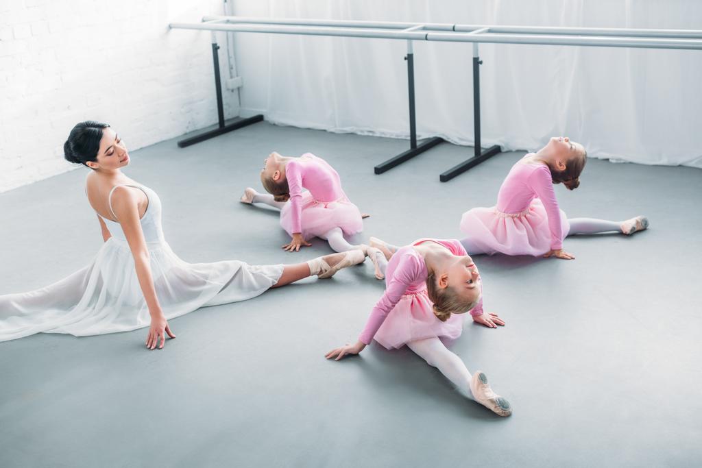 adorable little ballerinas and young teacher stretching and exercising together in ballet school - Photo, Image