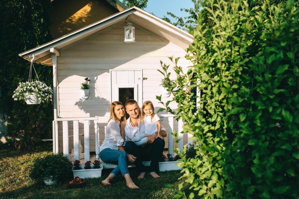 Χαμογελώντας οικογένεια με παιδάκι που κάθεστε μαζί στη βεράντα του μικρή εξοχική κατοικία - Φωτογραφία, εικόνα