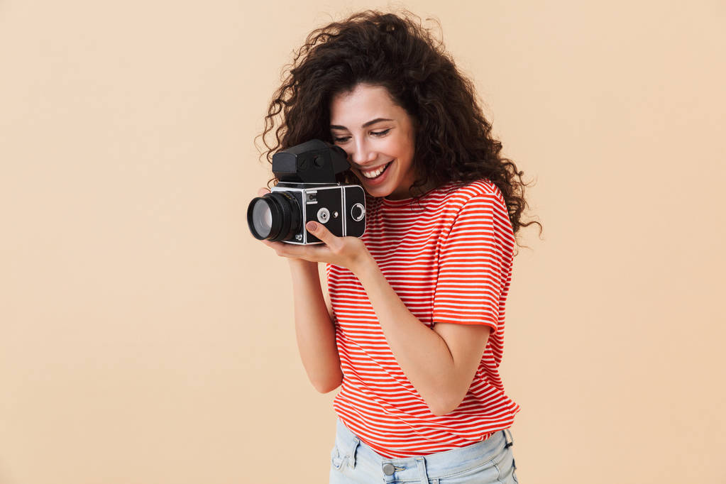Fotoğraf kamera tutarak bej renkli arka plan üzerinde izole güzel genç kıvırcık kadın fotoğrafçı. - Fotoğraf, Görsel
