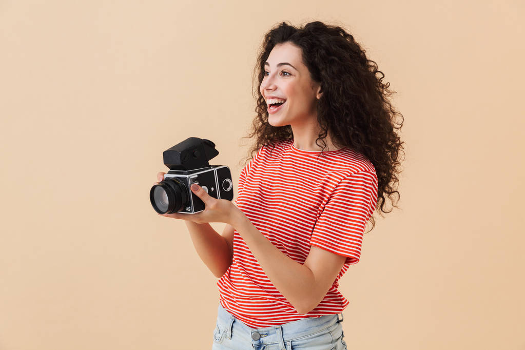 Obrázek hezká mladá žena kudrnaté fotograf izolované béžové pozadí drží fotoaparát. - Fotografie, Obrázek