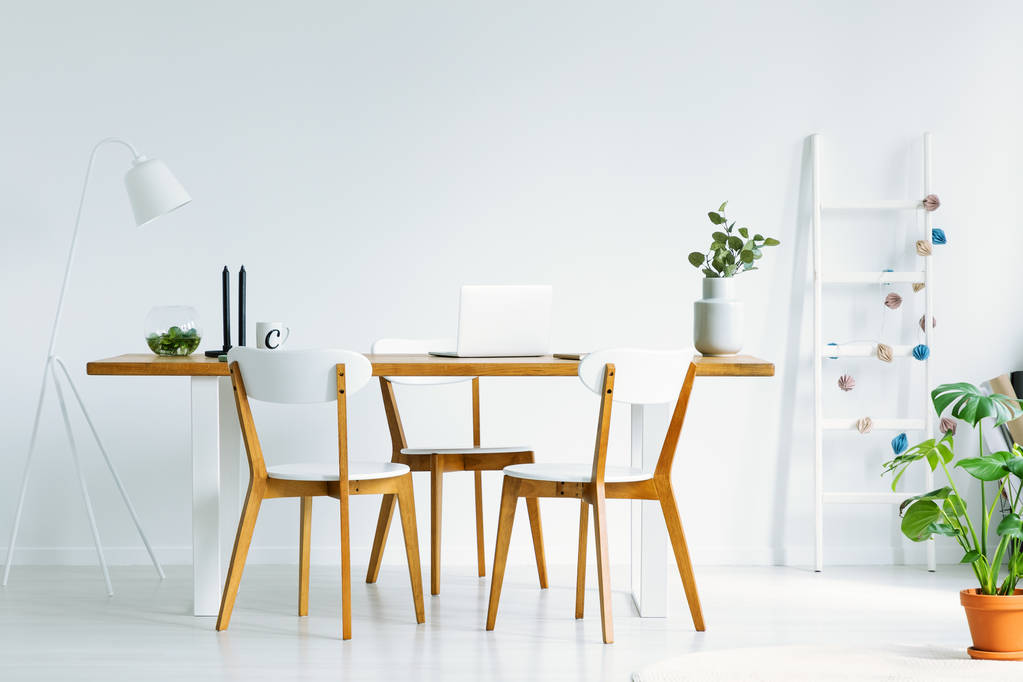 Яркий и естественный интерьер офиса с ноутбуком и тремя деревянными стульями вокруг простого стола. Настоящее фото
 - Фото, изображение