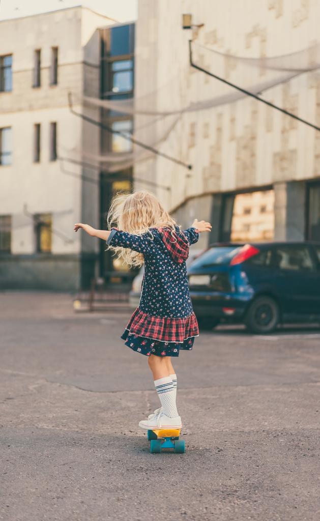 вид сзади на маленького ребенка, катающегося на скейтборде на городской улице
 - Фото, изображение