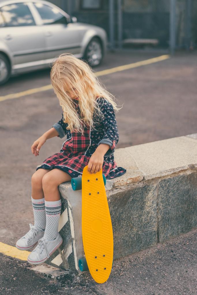 entzückendes Kind hält Skateboard in der Hand und sitzt an der Stadtstraße  - Foto, Bild
