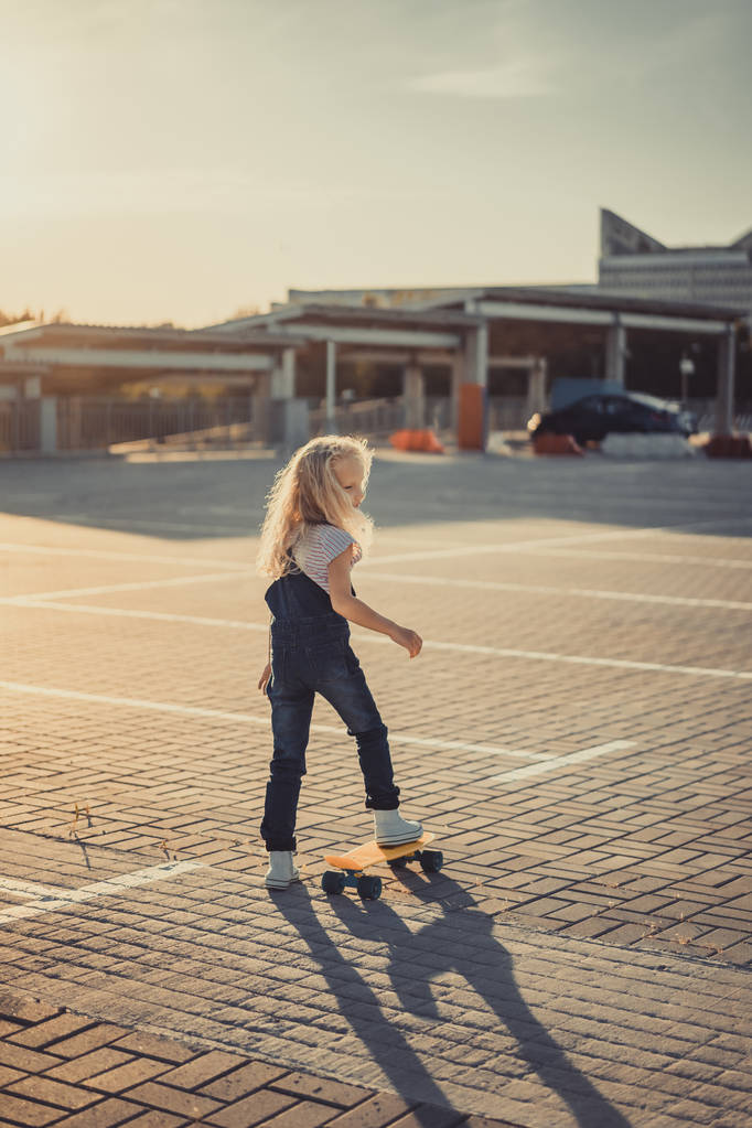 rear view of adorable kid standing with skateboard at parking lot  - Photo, Image