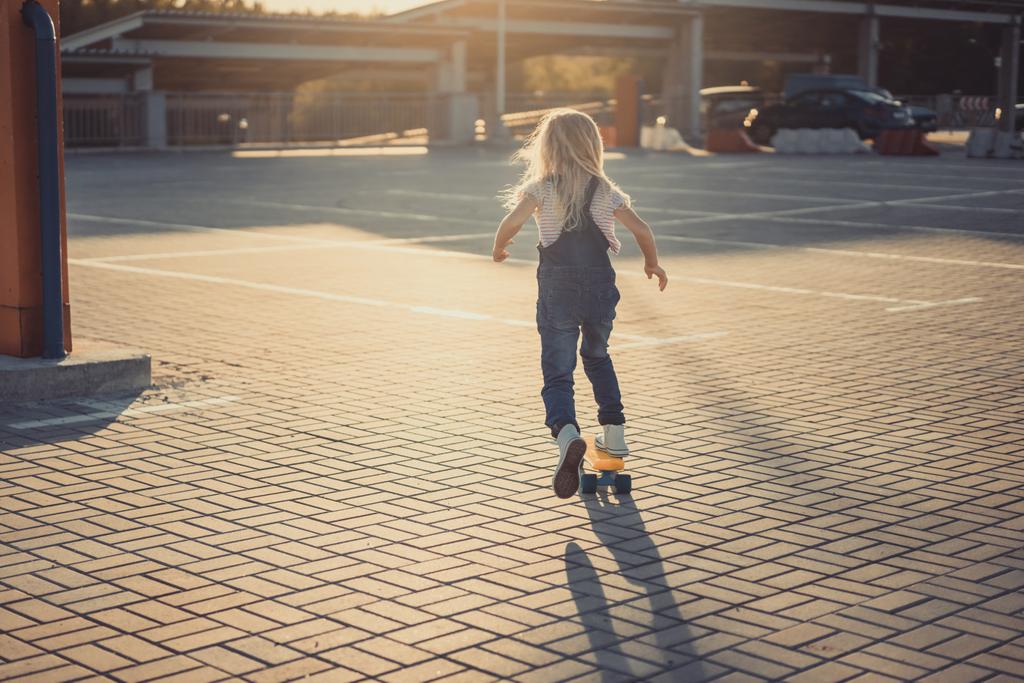 visão traseira de criança montando no skate no estacionamento
  - Foto, Imagem