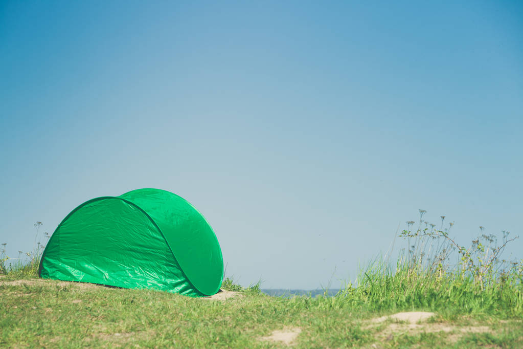 Tourismus und Erholung. kleines grünes Zelt im Naturgebiet umgeben von Wiese Wasser See. - Foto, Bild