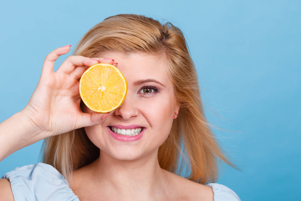 Mulher menina adolescente segurando metade de citrinos de limão amarelo na mão, cobrindo seu olho, em azul. Nutrição saudável da dieta. Felicidade conceito divertido
. - Foto, Imagem