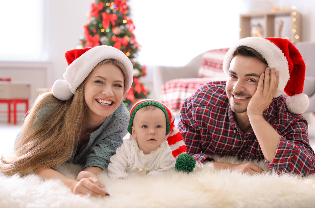 クリスマスの帽子を自宅で赤ちゃんと幸せなカップル - 写真・画像