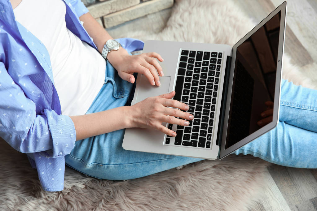 junge Frau benutzt Laptop, während sie drinnen auf dem Boden sitzt - Foto, Bild