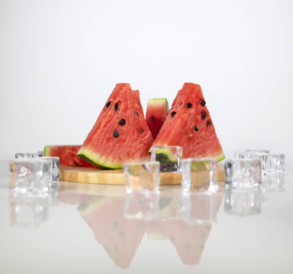 Berry watermeloen in water spatten. Witte achtergrond met verspreide ijsblokjes. - Foto, afbeelding