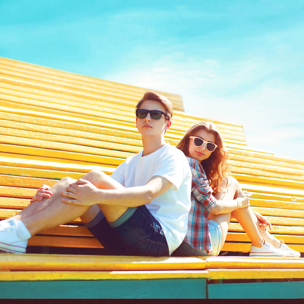 Модна молода пара сидить на лавці міського парку в сонячний літній день над блакитним небом
 - Фото, зображення