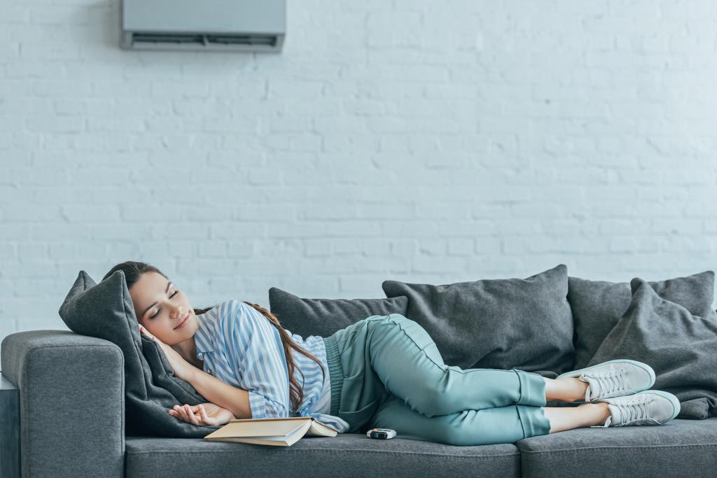 本と壁にエアコン、ソファで寝ている女性 - 写真・画像