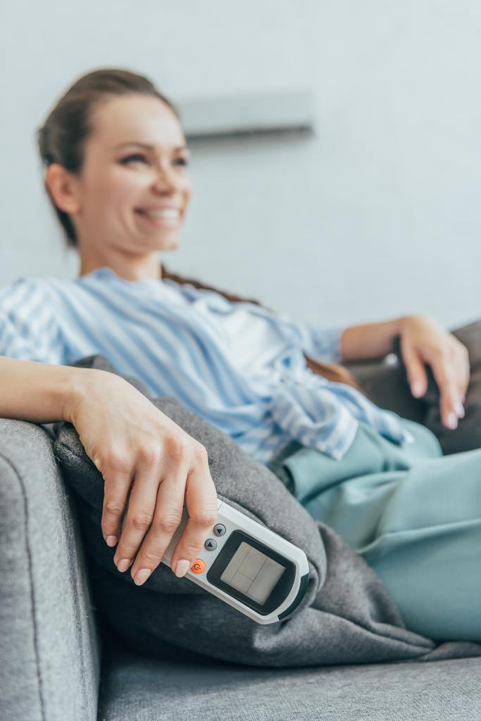 foco seletivo da mulher sentada no sofá com ar condicionado controle remoto
  - Foto, Imagem