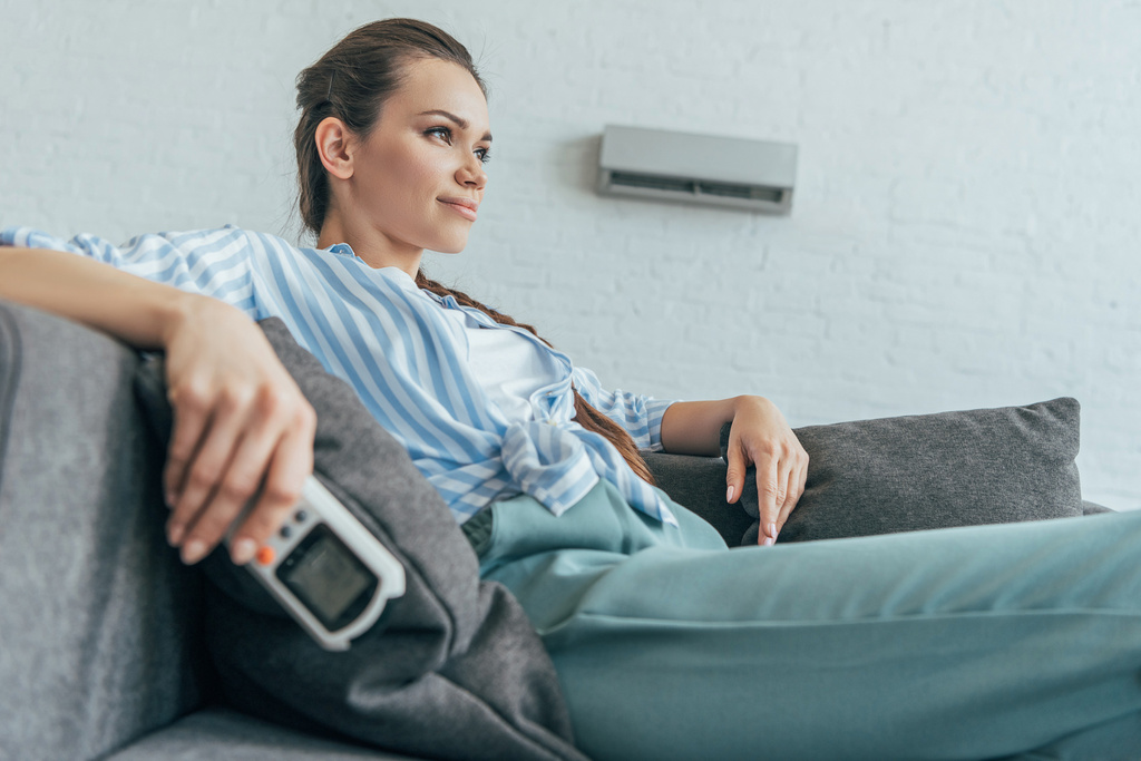 femme reposant sur canapé avec climatiseur télécommande, chaleur d'été
 - Photo, image