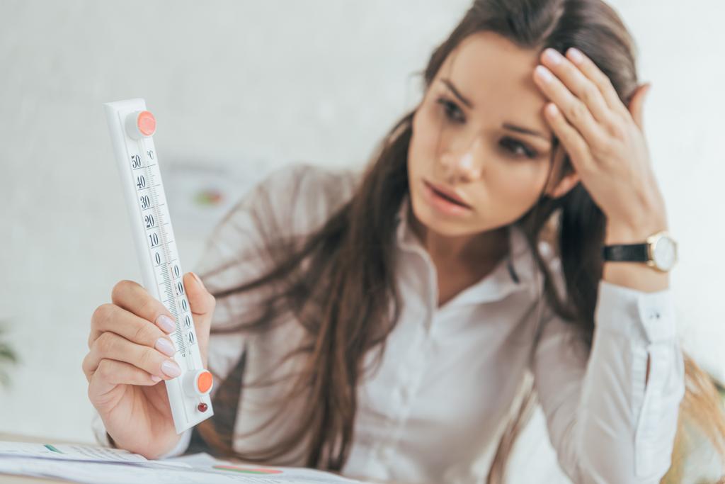 selective focus of businesswoman in hot office looking at thermometer - Photo, Image