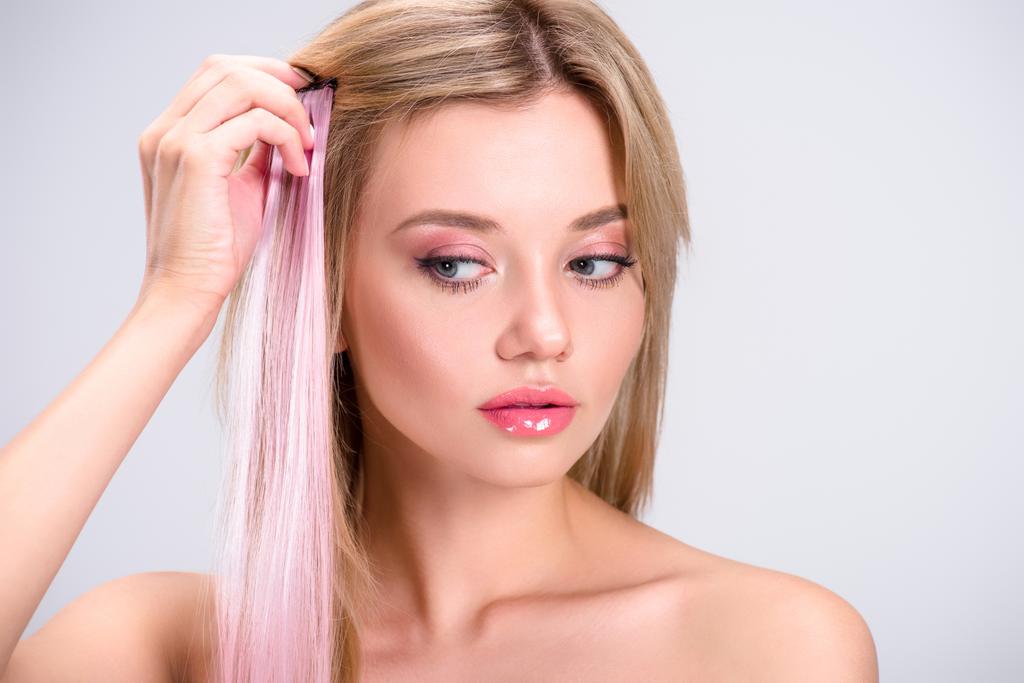κομψό νεαρή γυναίκα εφαρμόζοντας ροζ κλιπ μαλλιά σκέλος απομονωμένες σε γκρι - Φωτογραφία, εικόνα
