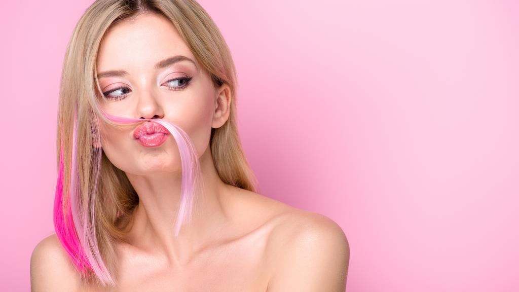 funny young woman making mustache with pink hair strand isolated on pink - Photo, Image
