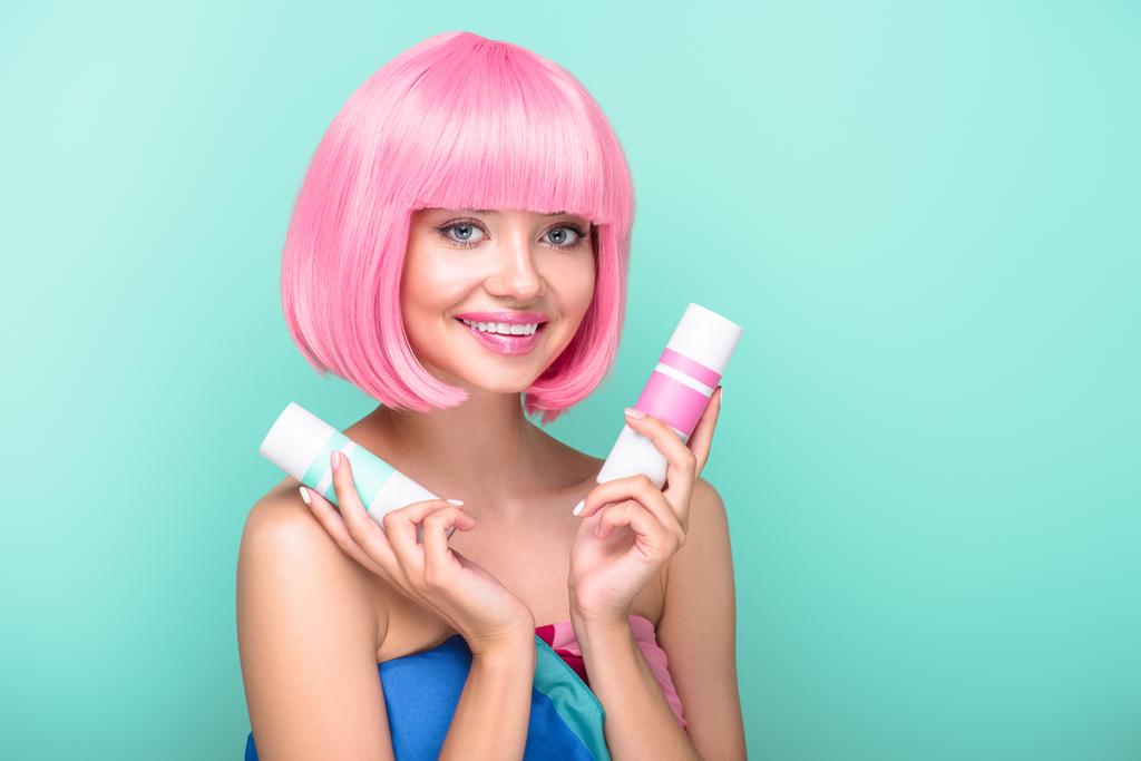 beautiful young woman with pink bob cut holding cans of coloring hair sprays isolated on turquoise - Photo, Image