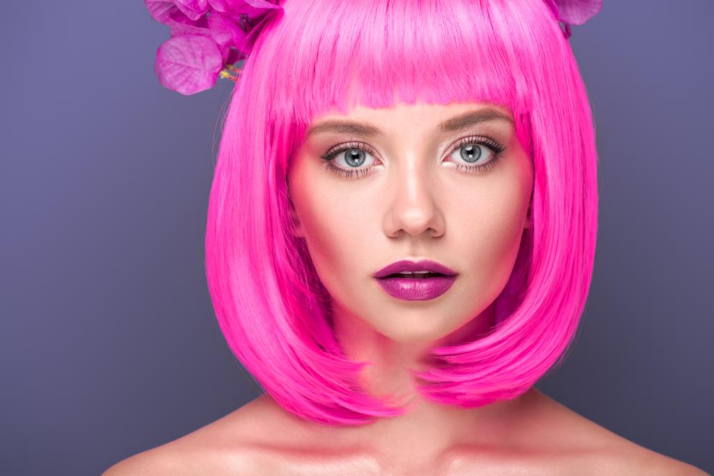 retrato de cerca de mujer joven atractiva con corte de color rosa bob y flores en el pelo mirando a la cámara aislada en violeta
 - Foto, imagen