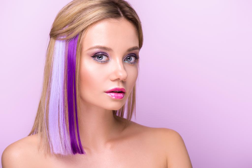 close-up portrait of stylish young woman with stylish makeup and purple hair strands looking at camera isolated on purple - Photo, Image