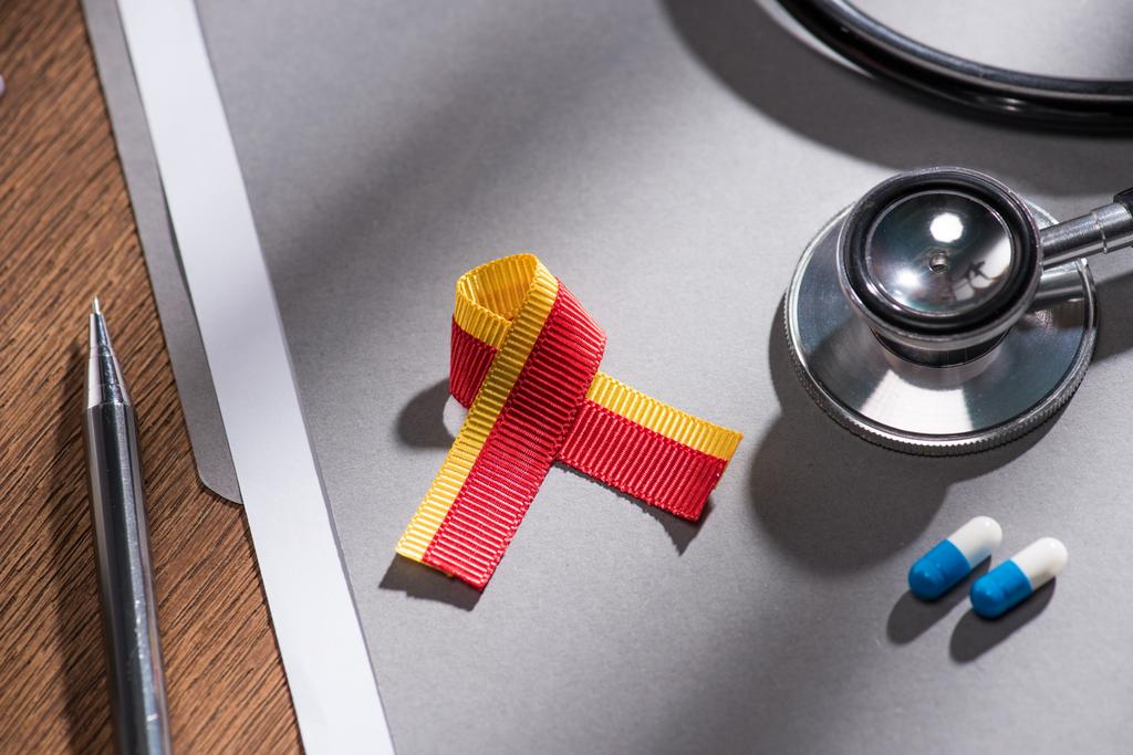 selective focus of ribbon, stethoscope, pills and folder with pen on table, world hepatitis day concept - Photo, Image