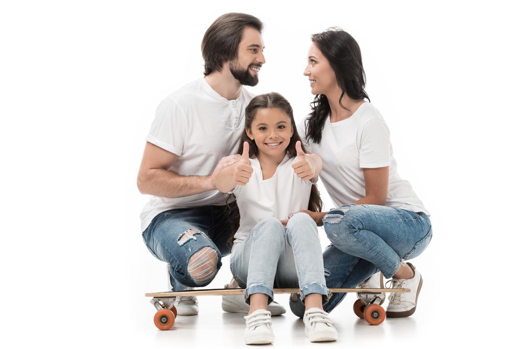 smiling kid sitting on skateboard and showing thumbs up with parents behind isolated on white - Photo, Image