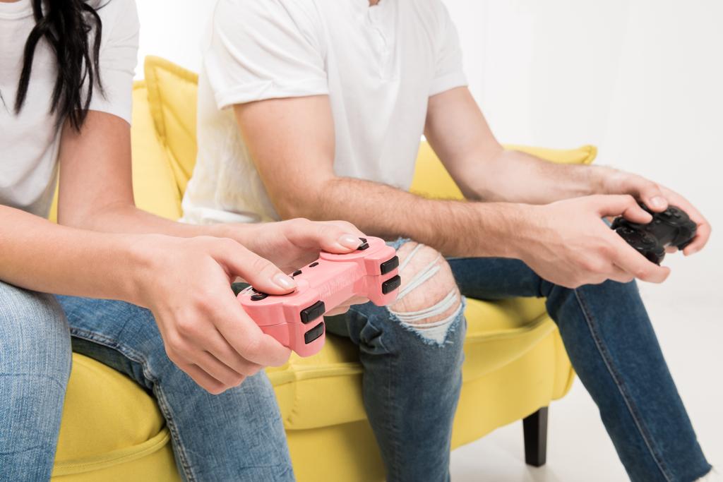 partial view of couple with gamepads sitting on sofa isolated on white - Photo, Image