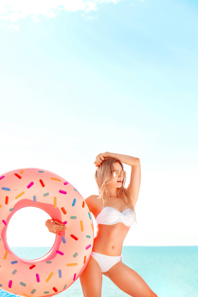Vacaciones de verano. Disfrutando de una mujer bronceadora en bikini blanco con colchón de rosquillas cerca del océano
. - Foto, imagen