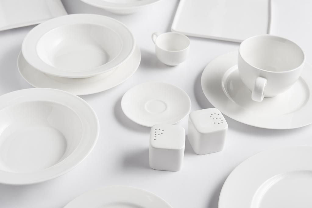 Nahaufnahme verschiedener Teller, Tasse, Schüssel, Salzkeller und Pfefferstreuer auf weißem Tisch  - Foto, Bild