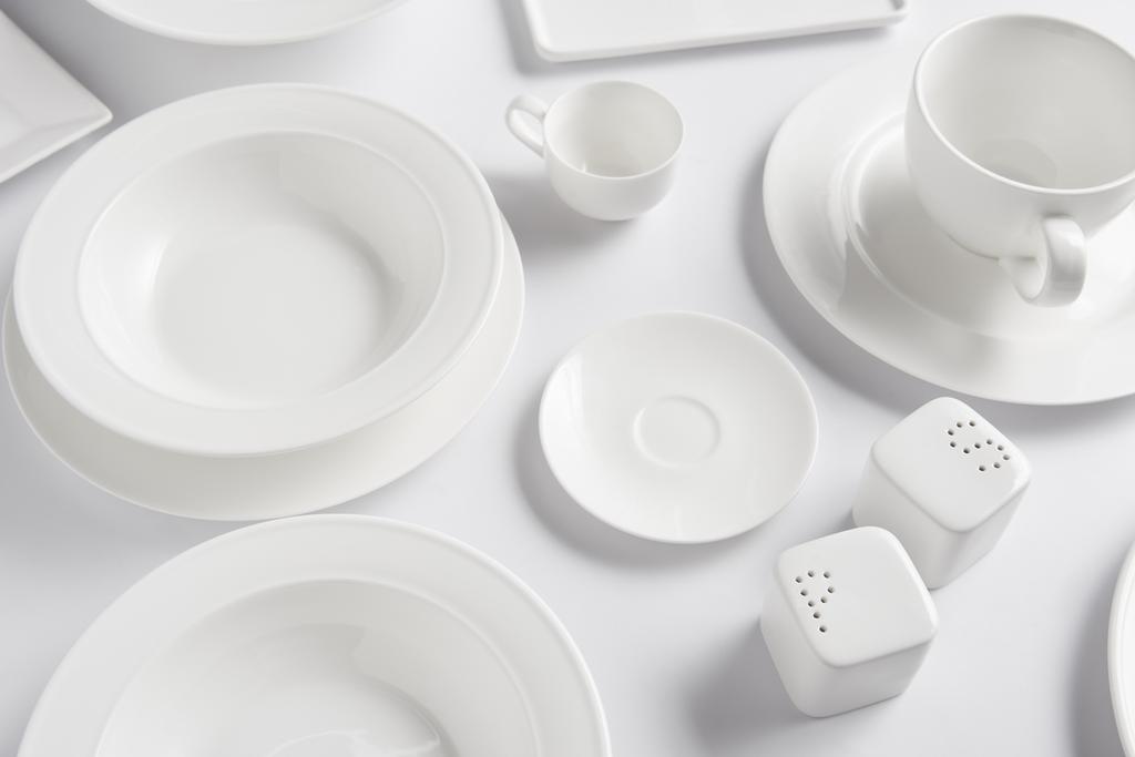Blick auf verschiedene Teller, Tasse, Schüssel, Salzkeller und Pfefferstreuer auf weißem Tisch  - Foto, Bild