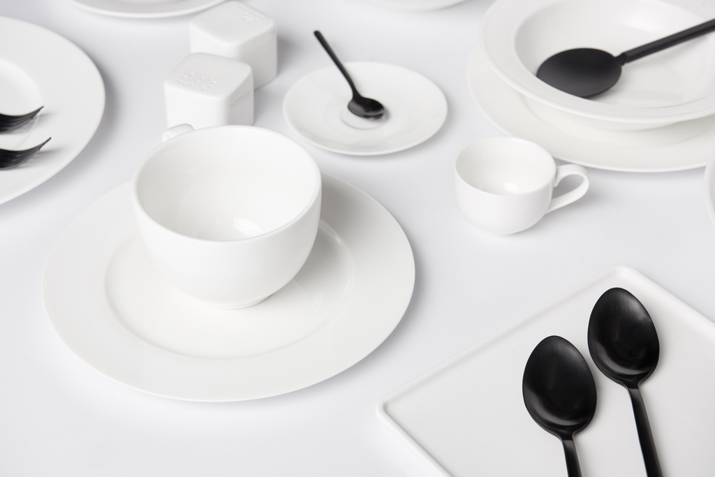 selective focus of different plates, cup, bowl, salad spoon, saltcellar and pepper caster, forks with spoons on white table - Photo, Image