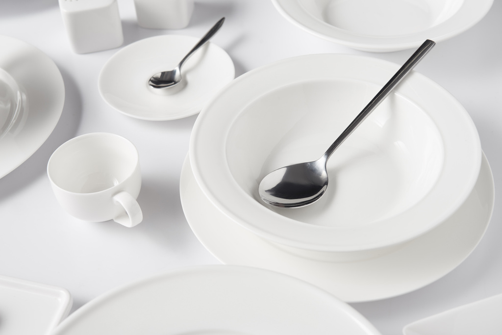 selektiver Fokus von Löffeln, verschiedenen Tellern und Tassen auf weißem Tisch - Foto, Bild