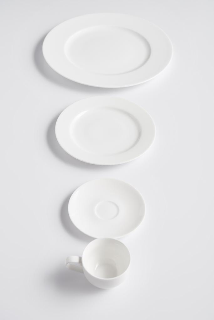селективный фокус расположения различных тарелок и чашки на белом столе
 - Фото, изображение