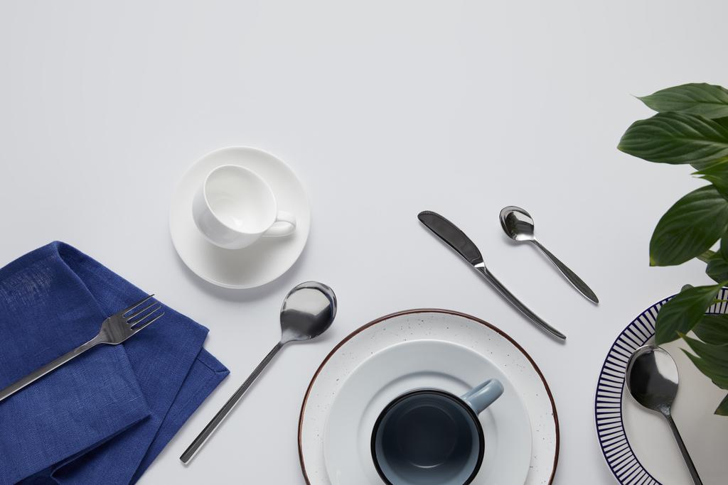 vista superior de hojas verdes, varios platos de cerámica, taza, toalla de cocina, tenedor, cucharas y cuchillo en la mesa blanca
  - Foto, imagen