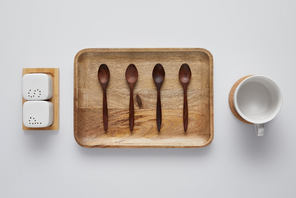 vista superior de la bandeja de madera arreglada con cucharas, bodega de sal, echador de pimienta y taza en la mesa blanca
 - Foto, Imagen
