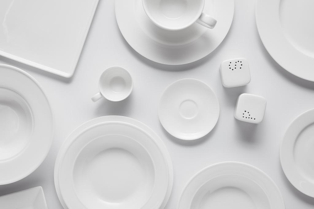 vista superior de diferentes platos, tazón, bodega de sal, echador de pimienta y taza en la mesa blanca
 - Foto, Imagen