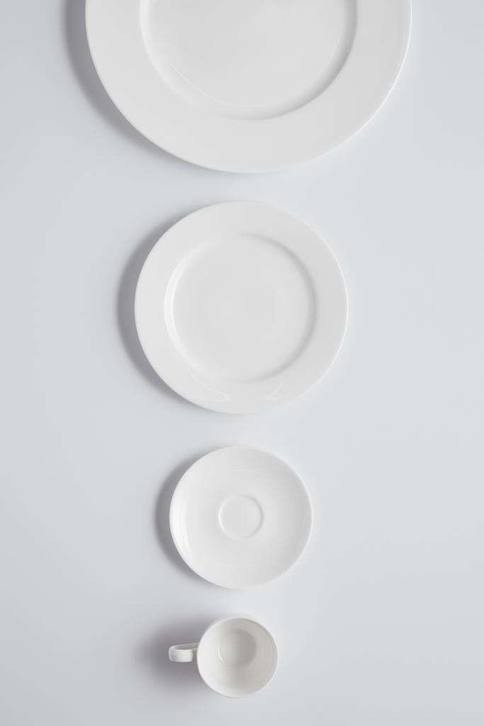 Вид сверху на различные тарелки и чашки подряд на белом столе, минималистичная концепция
 - Фото, изображение